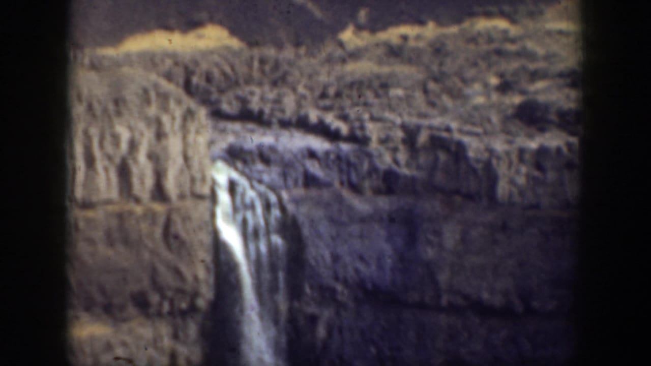 1937 California home-movie frame showing a waterfall descending through rugged layered cliffs with dark film-edge framing.