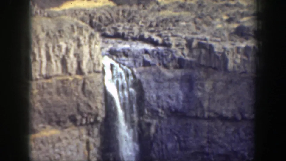 Closer 8mm view of a waterfall plunging down a rocky California cliff, with visible grain and faded color.