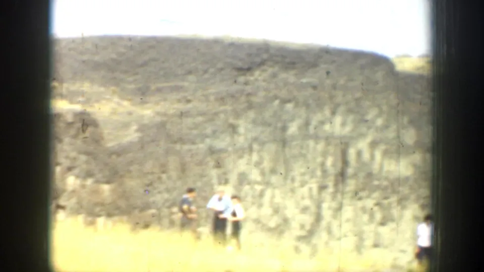Distant people walk through dry grass near a cliff in 1937 California home-movie footage.