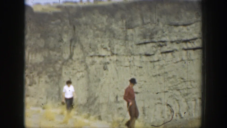 Two distant visitors pass a tall cliff wall in a 1937 California 8mm home-movie frame.