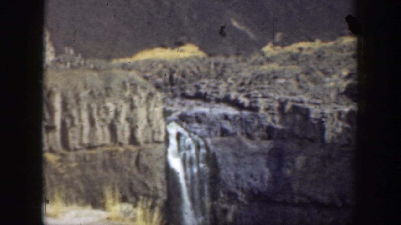 Waterfall dropping over a rocky cliff in a dry canyon landscape.