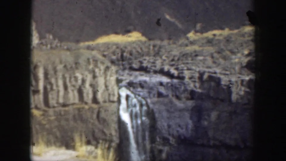 1937 California 8mm frame showing a waterfall descending from a rocky cliff into a rugged canyon setting.