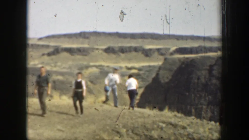 Several adults walk across dry, uneven California canyon terrain in a 1937 8mm home-movie frame.