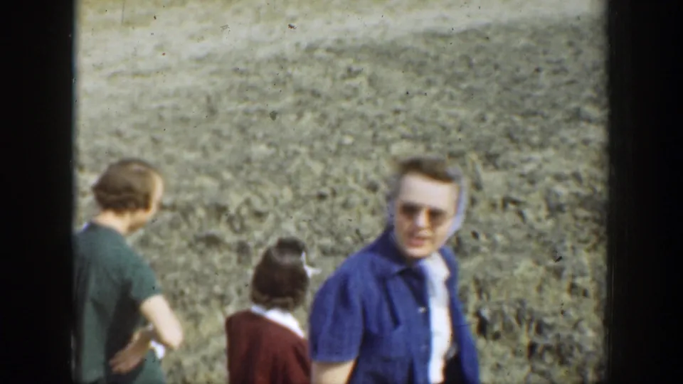 Three adults stand or turn near a textured canyon wall, including one face close to camera, in 1937 California home-movie footage.