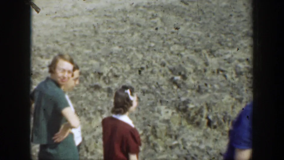 1937 California home-movie frame showing adults near a rocky wall, including a woman looking toward the camera.