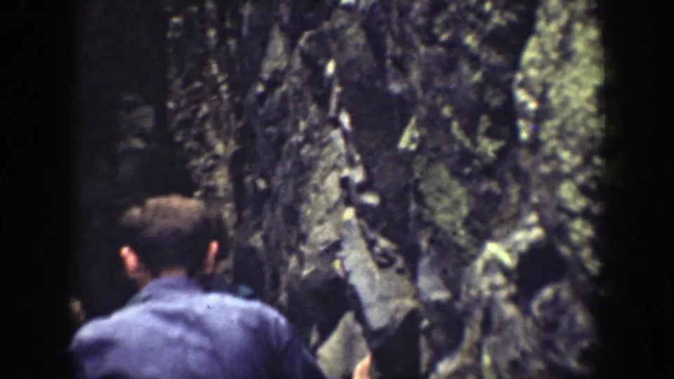 Hikers move single file through a shaded rocky passage in the California 1937 home-movie footage.