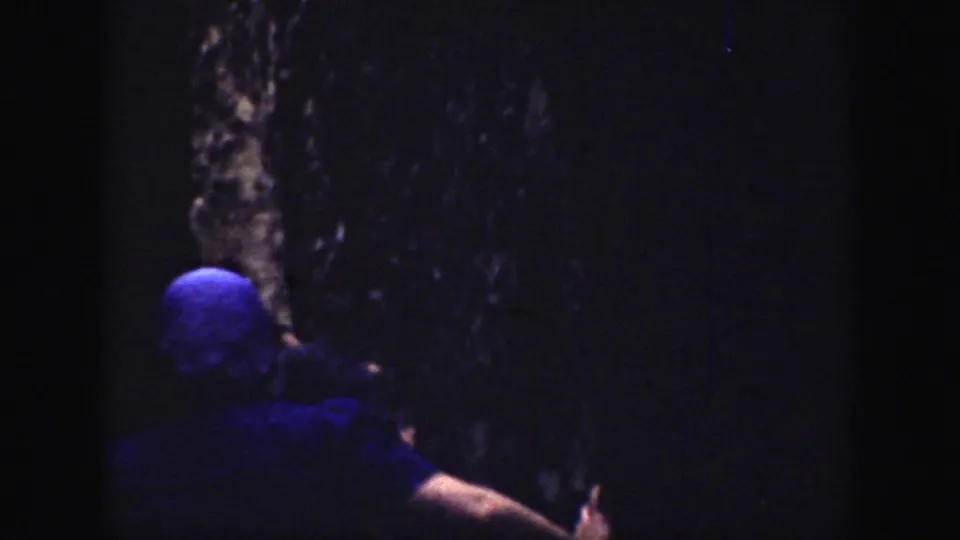 A dark 1937 California home-movie frame shows a hiker moving through a shadowed rock passage.