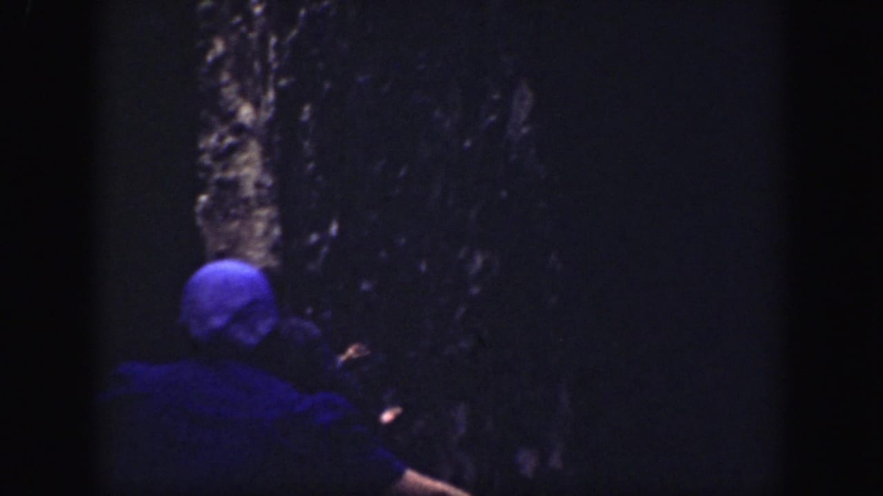 Tourists move through a dark narrow rock passage, with a person in a blue cap in the foreground.