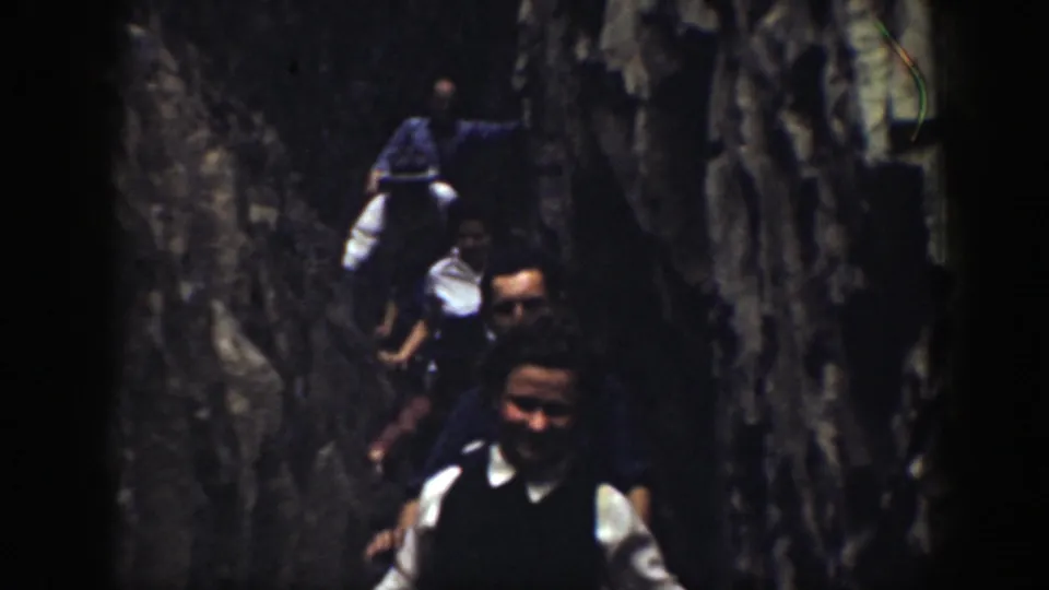 1937 home-movie frame of visitors walking through a confined California rock passage, some faces visible despite soft focus.