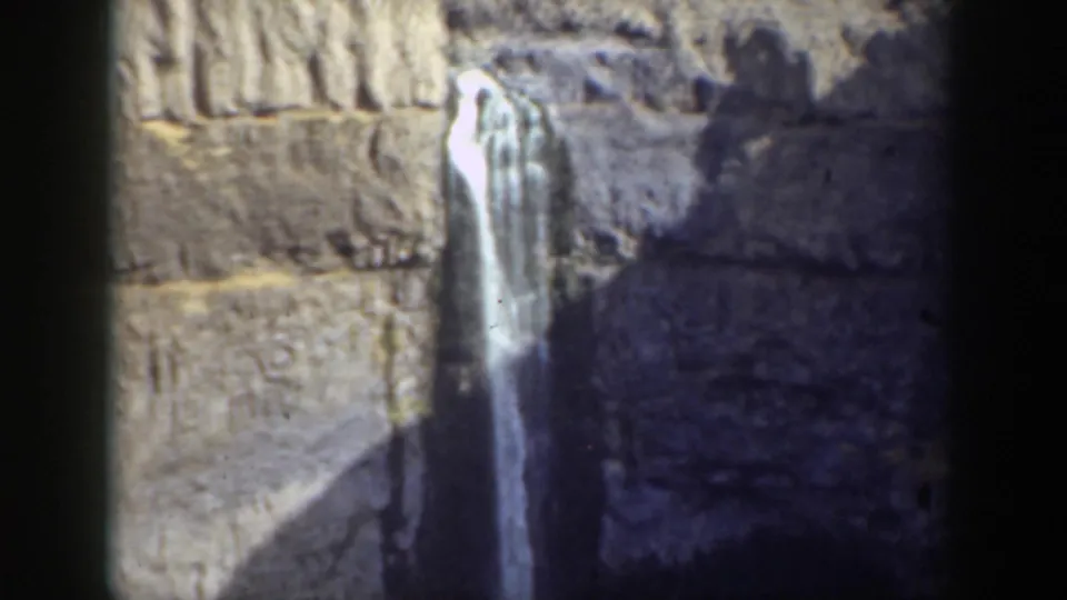 Small waterfall framed by textured California canyon rock, with shadow across the lower stone and no people visible in this frame.