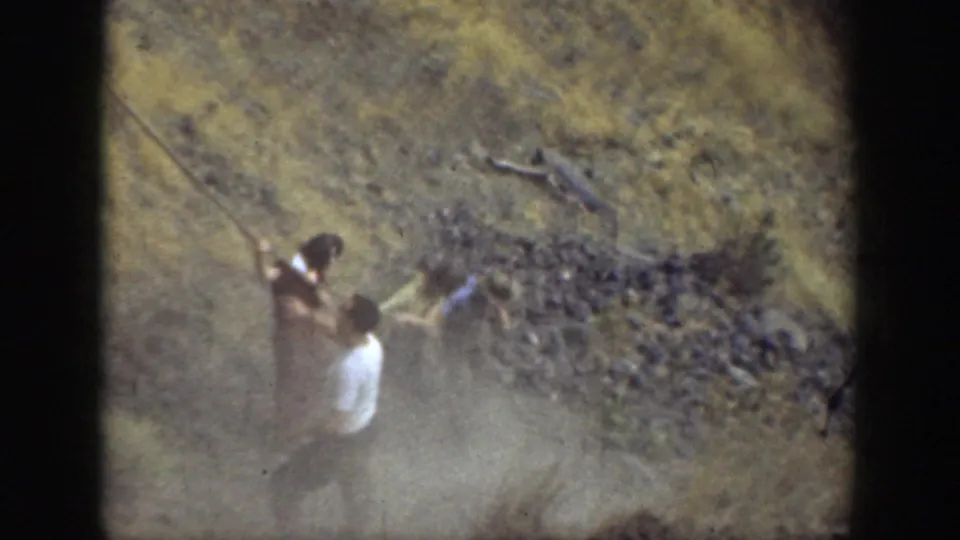 Two hikers appear on a steep, dusty rock slope in California, one near a rope or handhold.