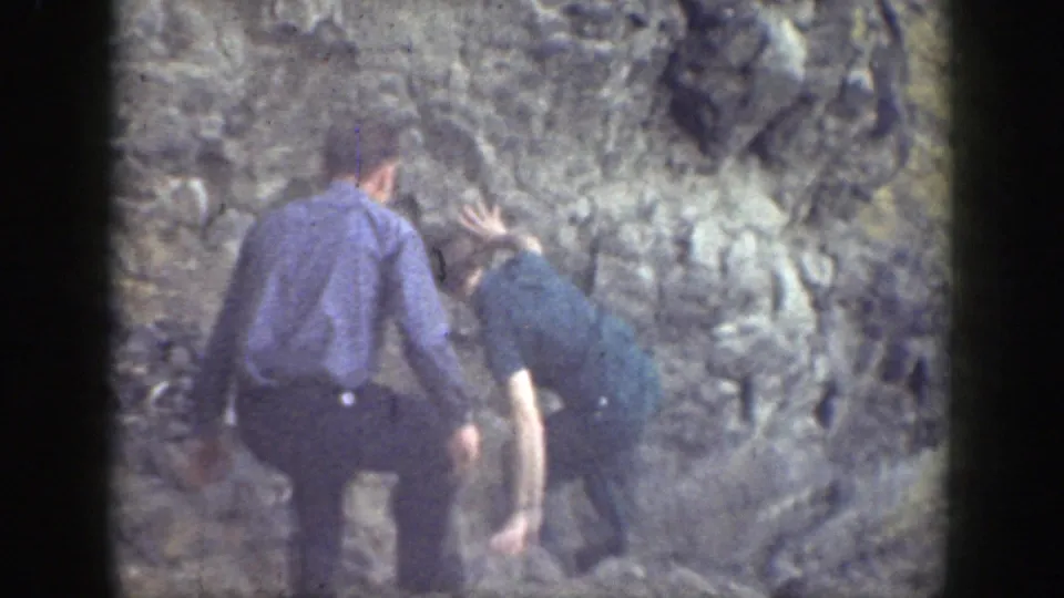 Two men in period clothing stand close to a rocky wall while navigating the trail in 1937 California footage.
