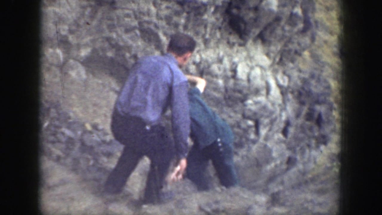 Adults on a rocky slope gather around a person low to the ground.