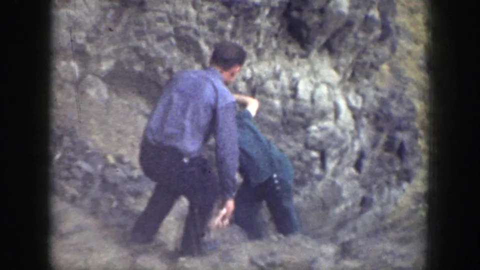1937 California home-movie frame showing adults on a steep rocky hillside assisting someone who appears to have fallen.