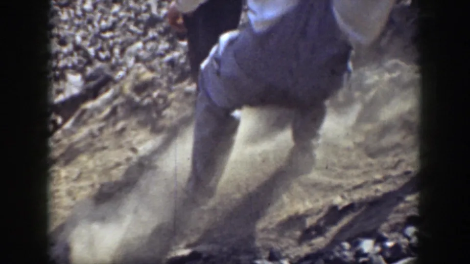 1937 California home-movie frame showing a close, cropped view of a person moving up loose gravel with dust around their feet.