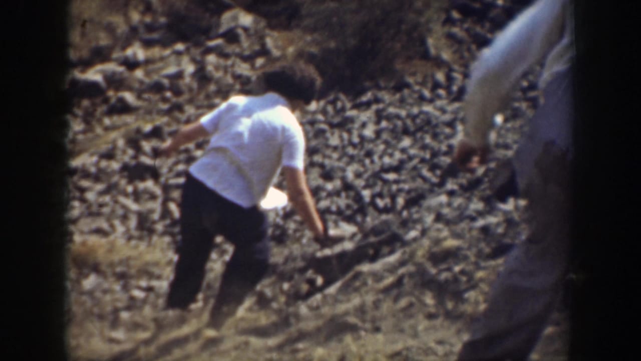 Person in a white shirt descends a steep rocky hillside.