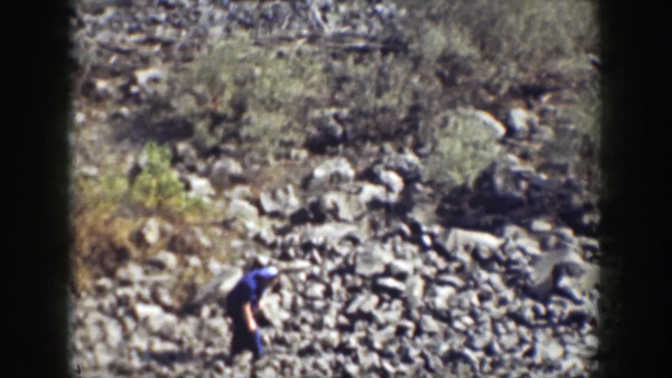A distant hiker crosses loose stones and sparse vegetation in dated 1937 California 8mm footage.