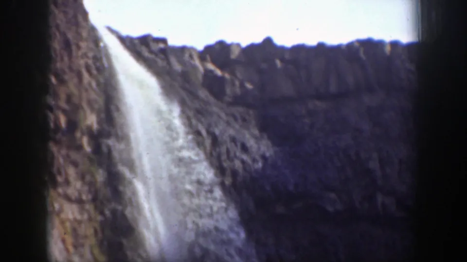A broader home-movie view of a California waterfall descending over rugged cliffs in strong sunlight and shadow.