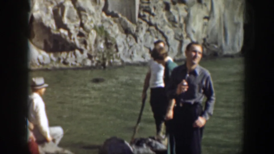 Home-movie frame of adults gathered beside the water at a 1937 California waterfall location, with cliffs behind them.