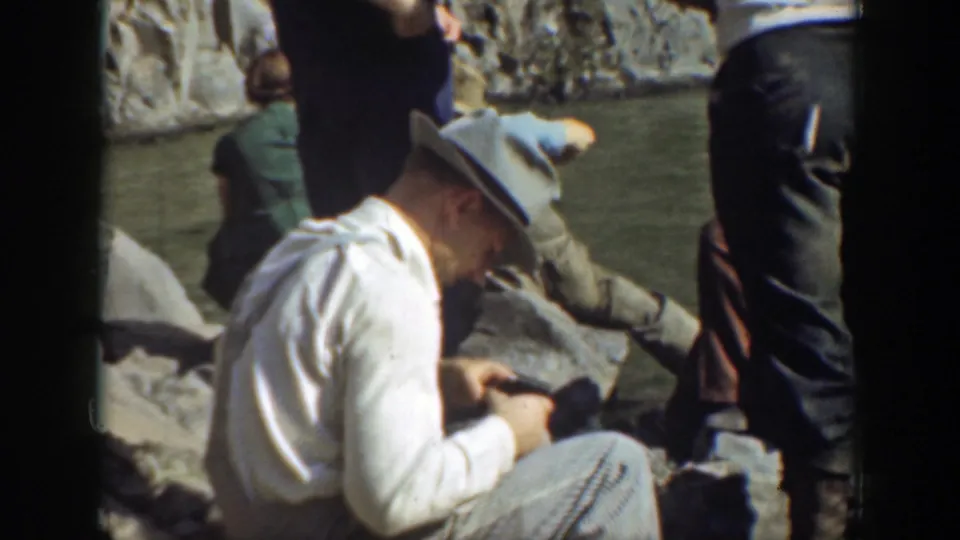 In 1937 California home-movie footage, a man in a fedora sits by rocks near water as other adults gather around him.