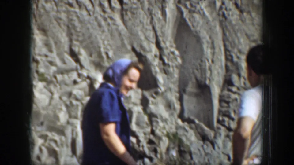 A woman in a blue headscarf smiles near a rocky cliff face during the 1930s California waterfall visit.