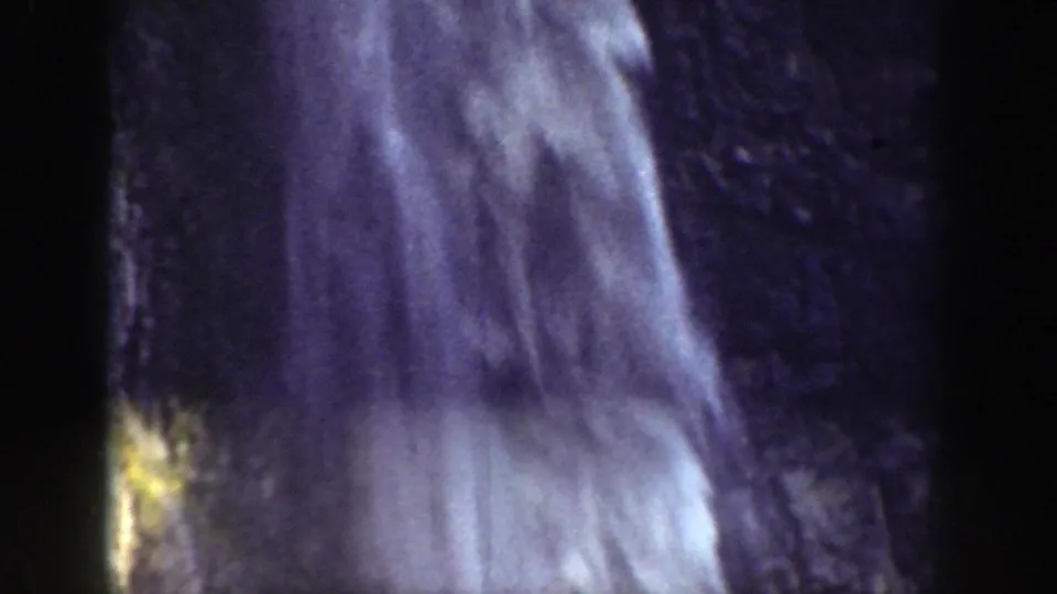 A close-up view shows the waterfall streaming down a dark rock face, with soft focus and 8mm film grain.