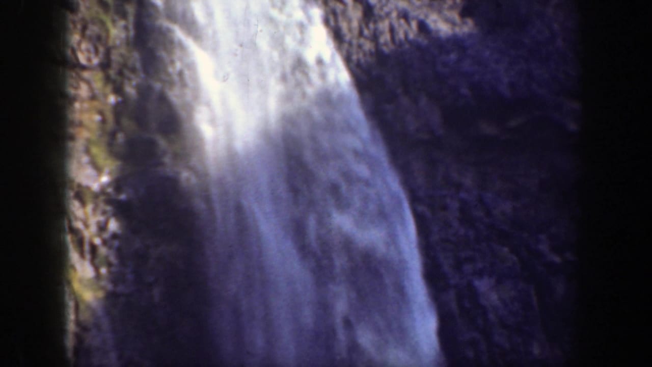 Waterfall dropping down a dark rocky cliff with bright spray and soft film grain.