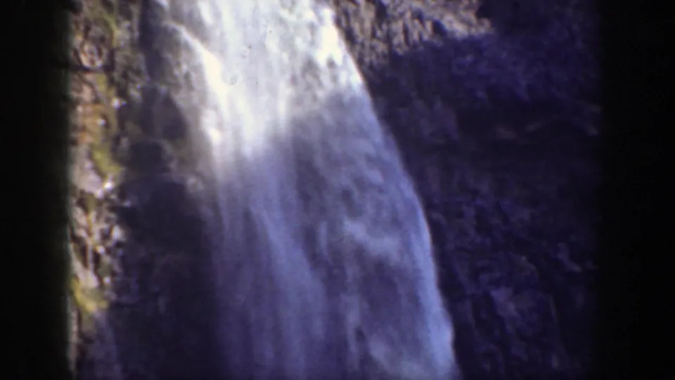 1937 California 8mm frame showing a waterfall descending a rugged cliff face with pale spray and dark rock texture.