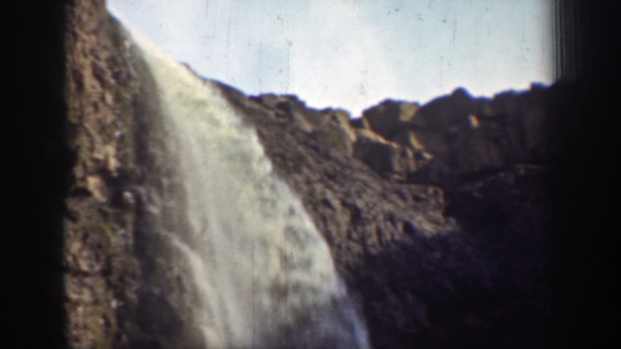 Waterfall flowing over a rocky ledge beneath bright sky, with dark frame edges.