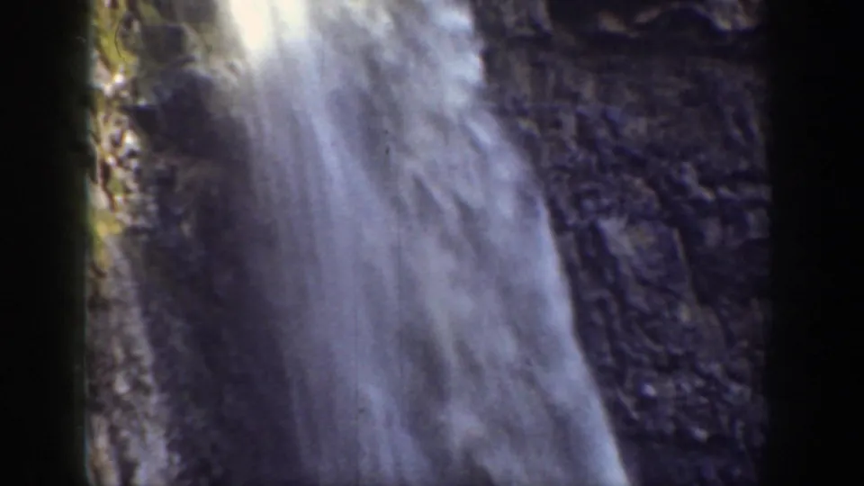 1937 California home-movie frame showing waterfall spray against a dark, textured cliff, with soft focus and faded color.