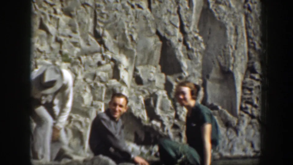Home-movie frame of visitors resting near a rocky wall in California, with faces partly visible.