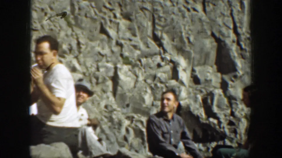 1937 California 8mm frame showing several men resting against a rock face, with one man in a white shirt smoking near the left edge.