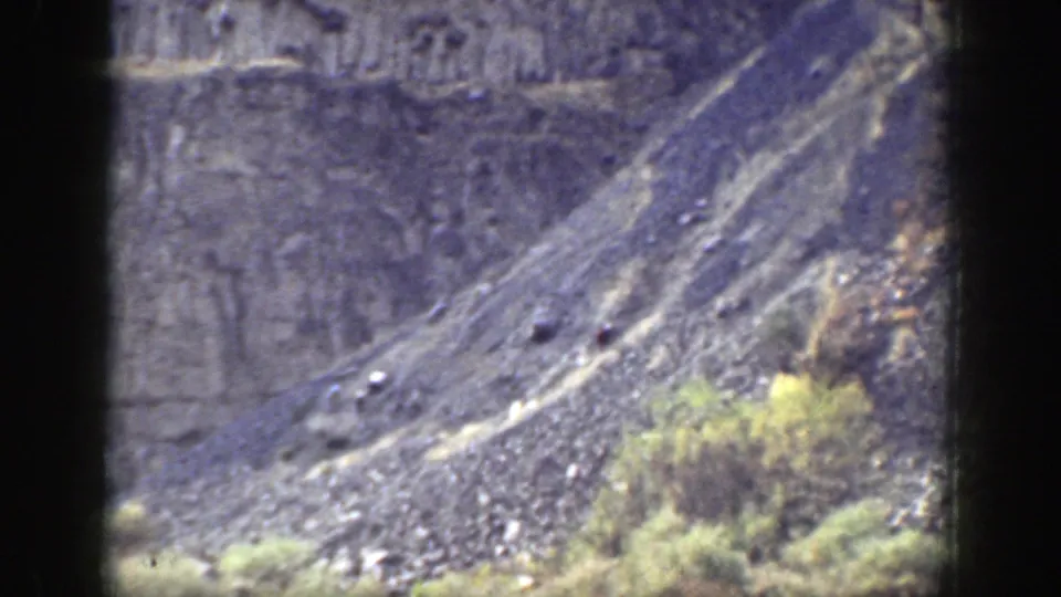 The camera follows the rocky California incline, showing loose stone, canyon walls, and sparse vegetation after the throw.