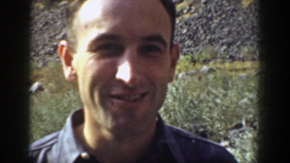 A close view shows the man smiling toward the camera, with the rugged California slope visible behind him.