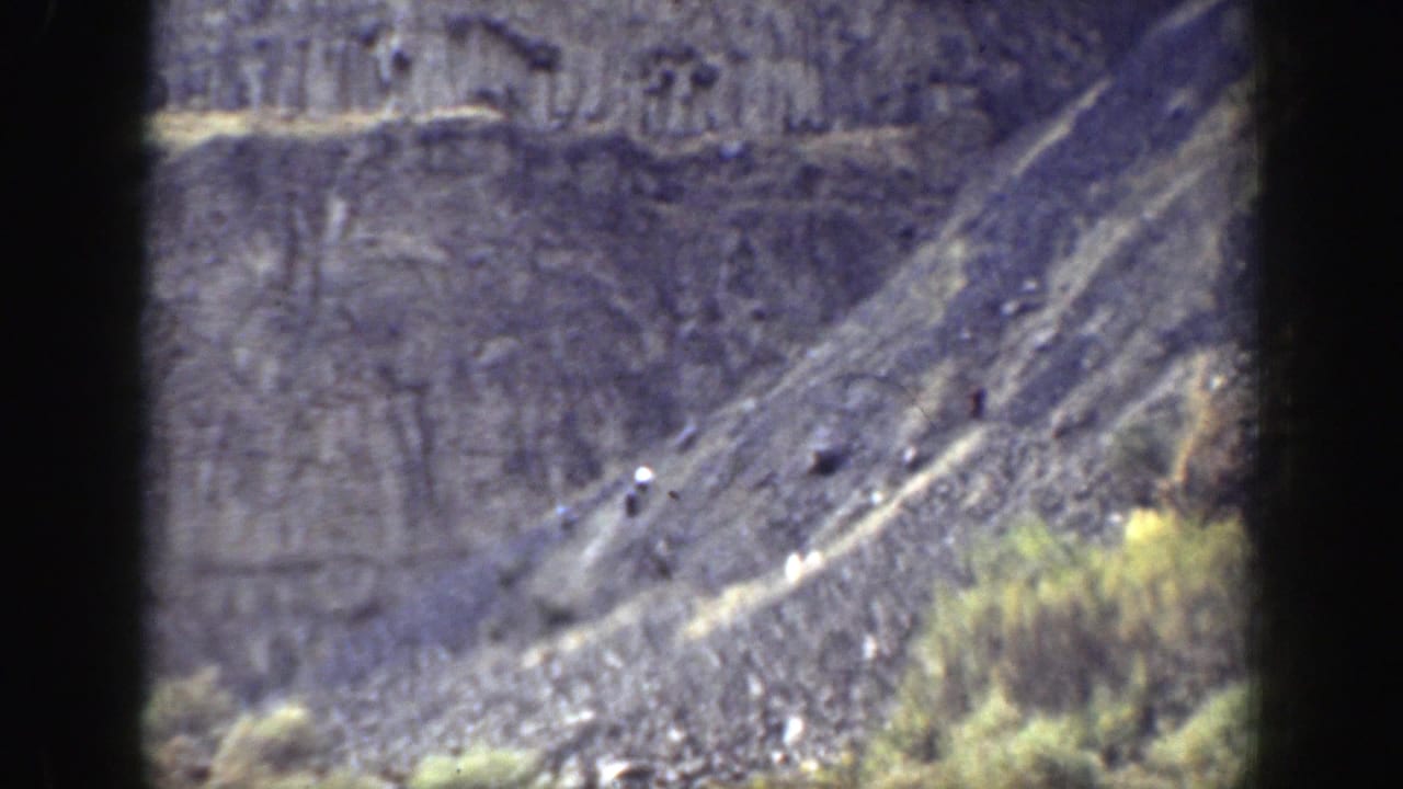 1937 California 8mm frame showing a distant rugged hillside with dry grass, scrub, layered rock, and dark scan borders.