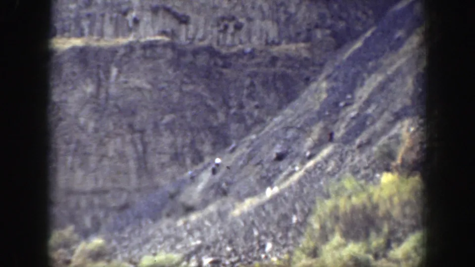 1937 California 8mm frame showing a distant rugged hillside with dry grass, scrub, layered rock, and dark scan borders.