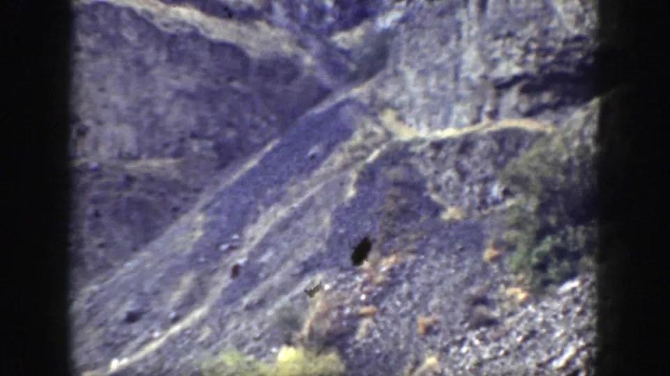 Rugged California mountainside in soft 8mm color, with pale paths crossing rock and scrub-covered slopes.