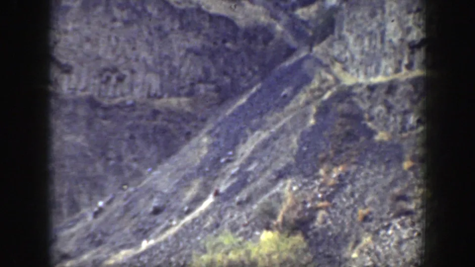 1937 California mountain landscape in 8mm color, showing diagonal trails across rocky terrain and scattered shrubs.