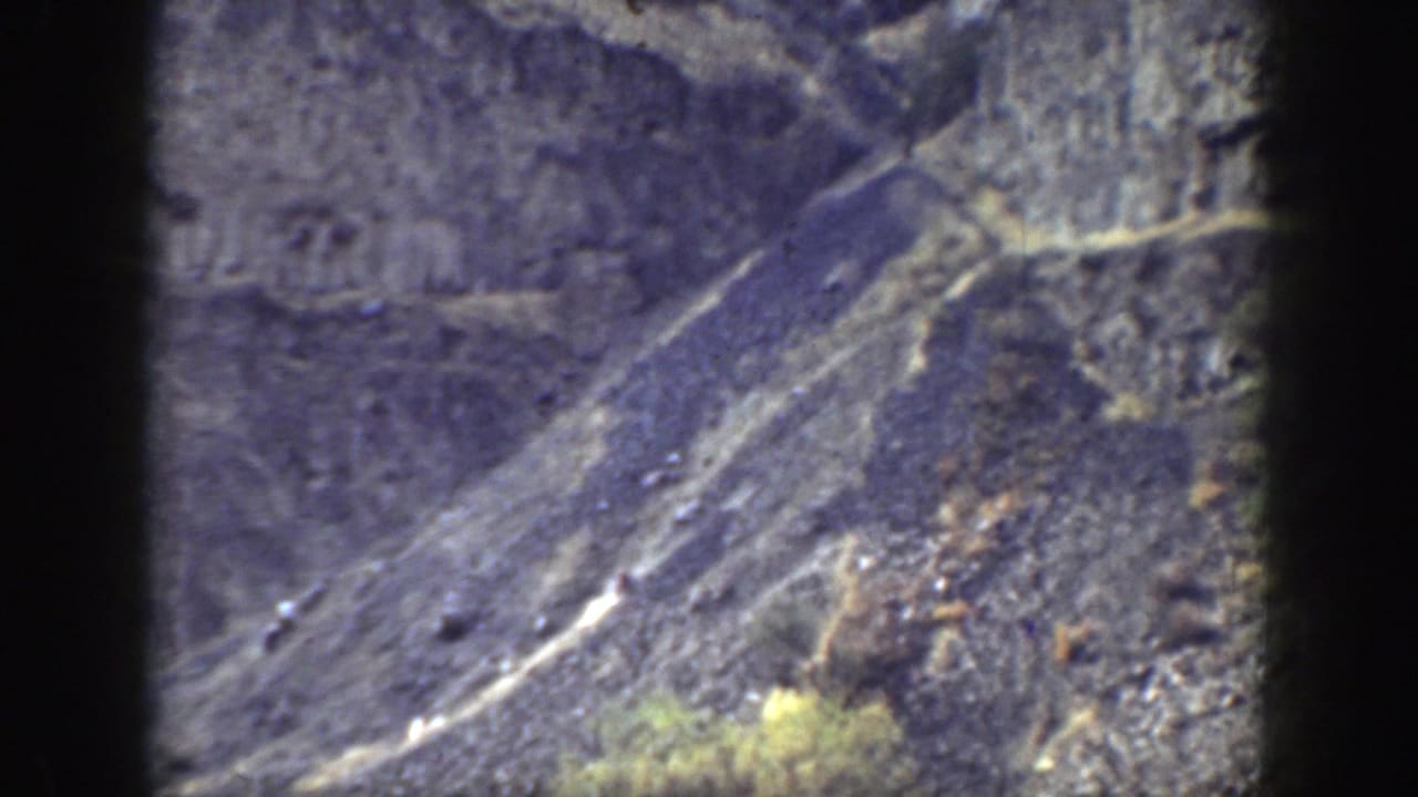 Rocky mountain slope with a faint path and dry vegetation in bright daylight.