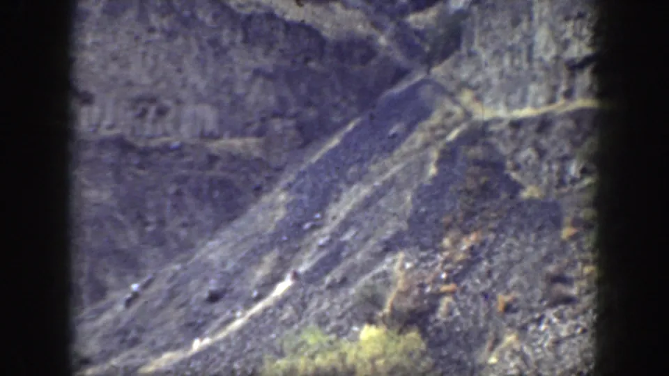 1937 California 8mm frame showing a rugged mountain slope, exposed rock, and sparse dry vegetation from a distant viewpoint.