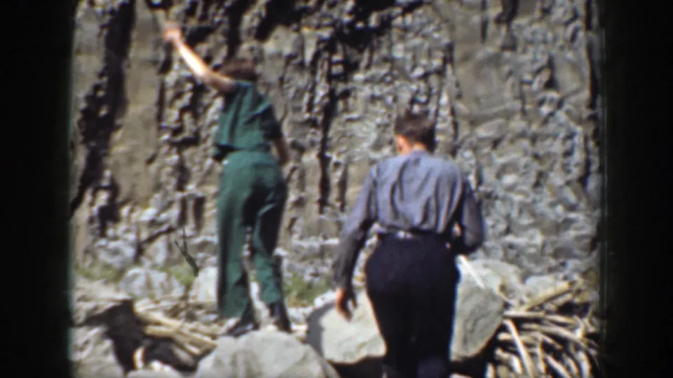 Two adults in period clothing move through rocky terrain below a cliff face in this 1937 California home-movie frame.