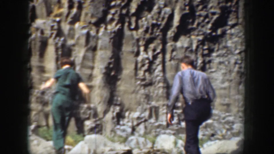 Two adults walk away along rough cliffside rocks in California, captured in soft, grainy 8mm home-movie footage from 1937.