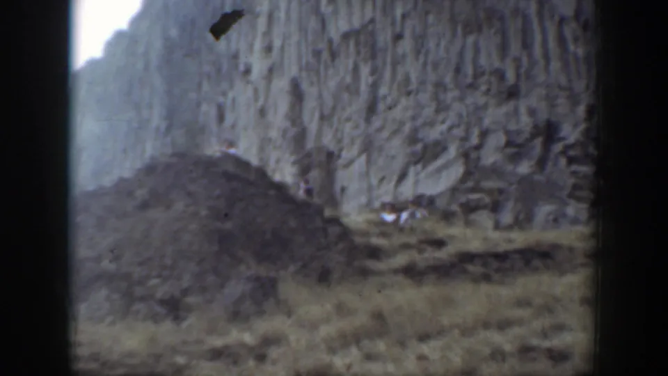 Rocky canyon-like terrain in the California home movie, with steep cliffs, scrub, and a dark mound of loose stone.