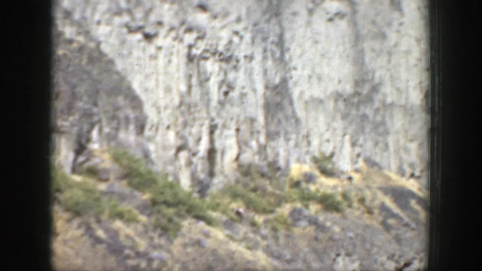 1937 California home-movie frame showing a sunlit striated cliff, rocky slope, scrub vegetation, and dark 8mm frame edges.
