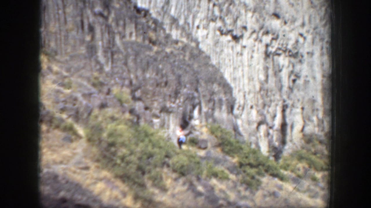 Distant person in a white shirt walking near a grey rocky canyon wall.