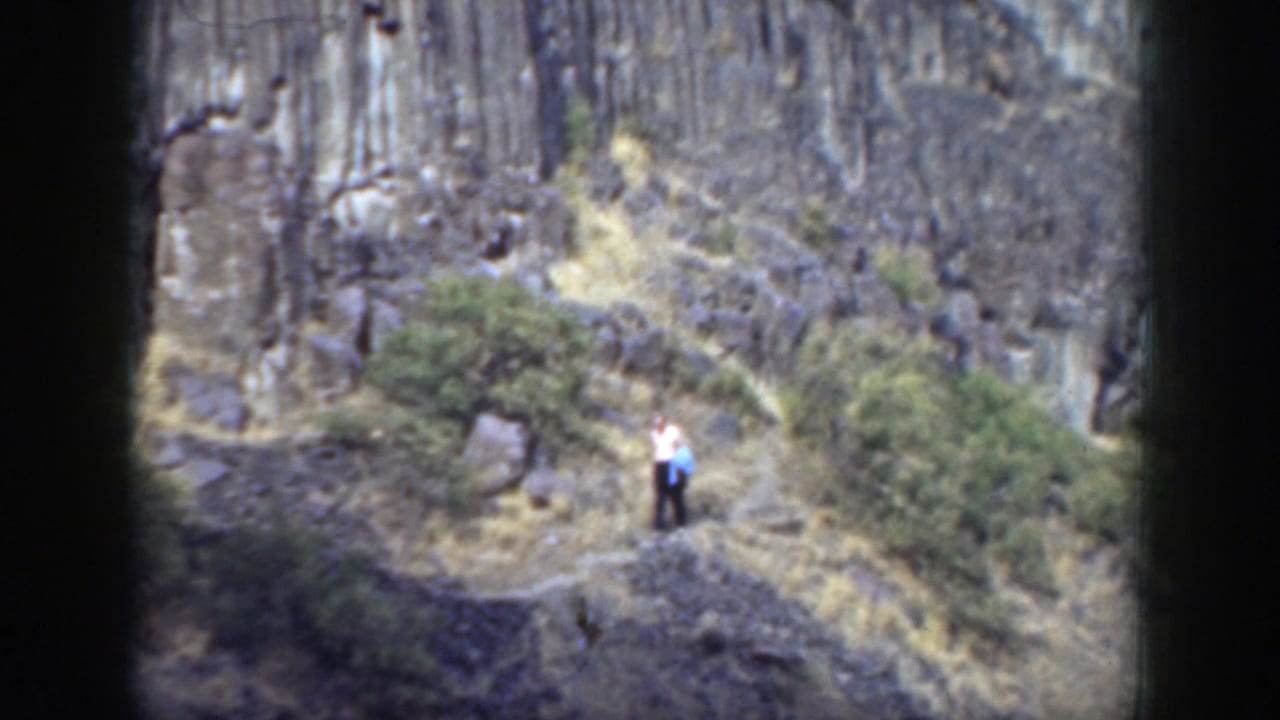 Man standing on a rocky mountain trail below a steep cliff face.