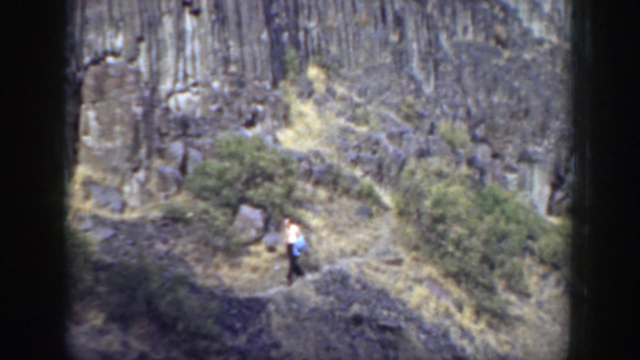Man walking along a narrow trail across a rocky hillside.