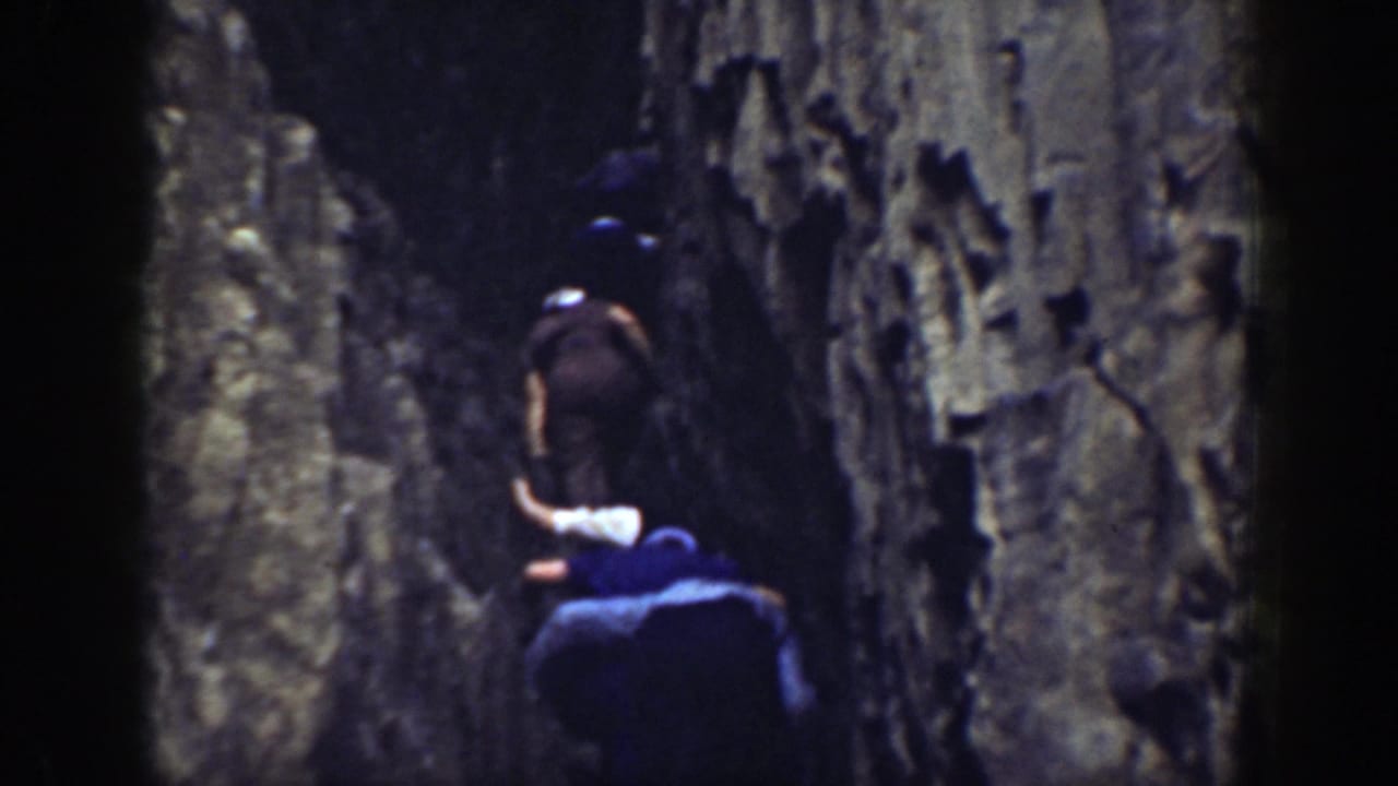 Two men climbing upward through a narrow rock crevice.