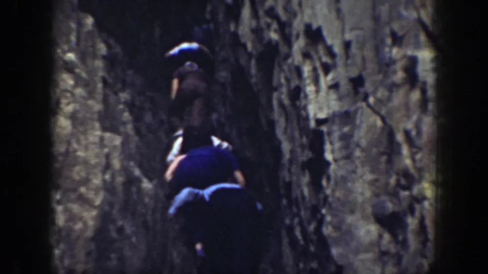 Two men continue climbing in a tight rocky passage in 1937 California footage.