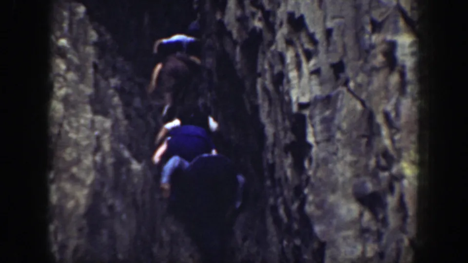 Two men in period outdoor clothing climb close against a rugged California rock face.